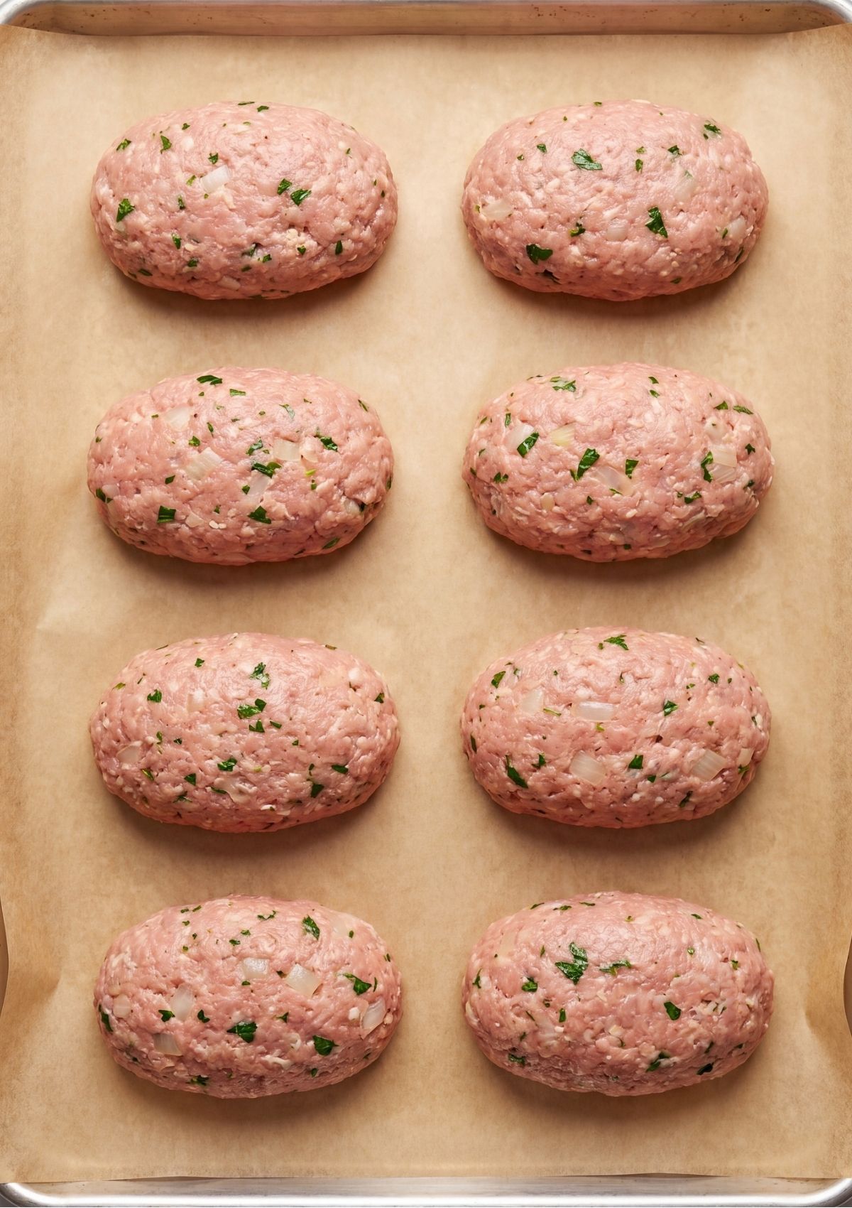 Eight raw ground turkey meatloaf portions shaped into small uniform oval loaves and arranged on a parchment-lined baking pan