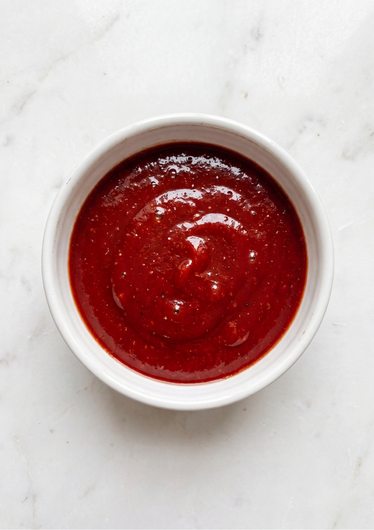 A small white bowl filled with a smooth, thick red tomato-based glaze for the turkey meatloaf.