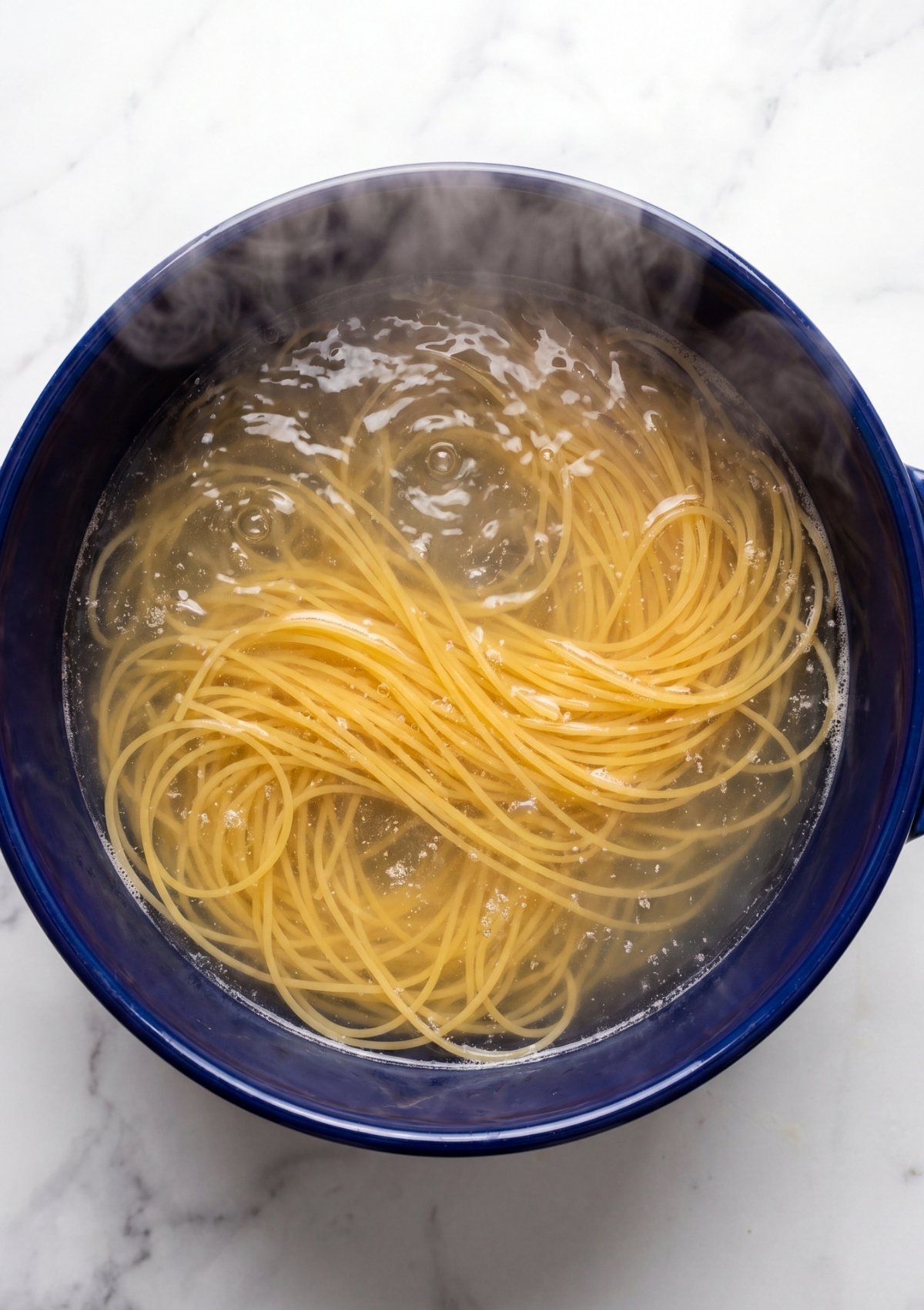 Long spaghetti noodles boiling in a blue pot of water with steam rising, captured on a light background.