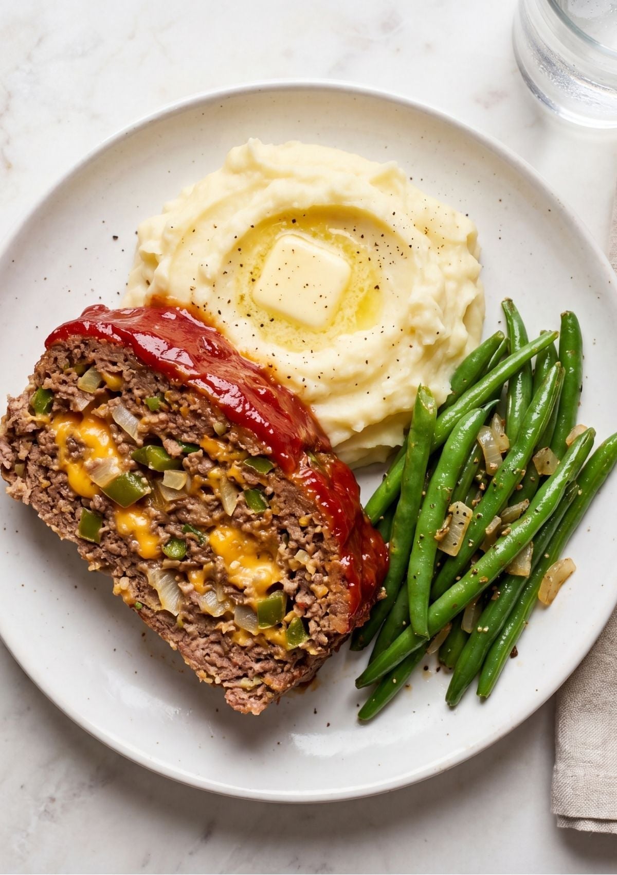 A detailed view of a meatloaf slice revealing melted cheddar cheese and green peppers inside.