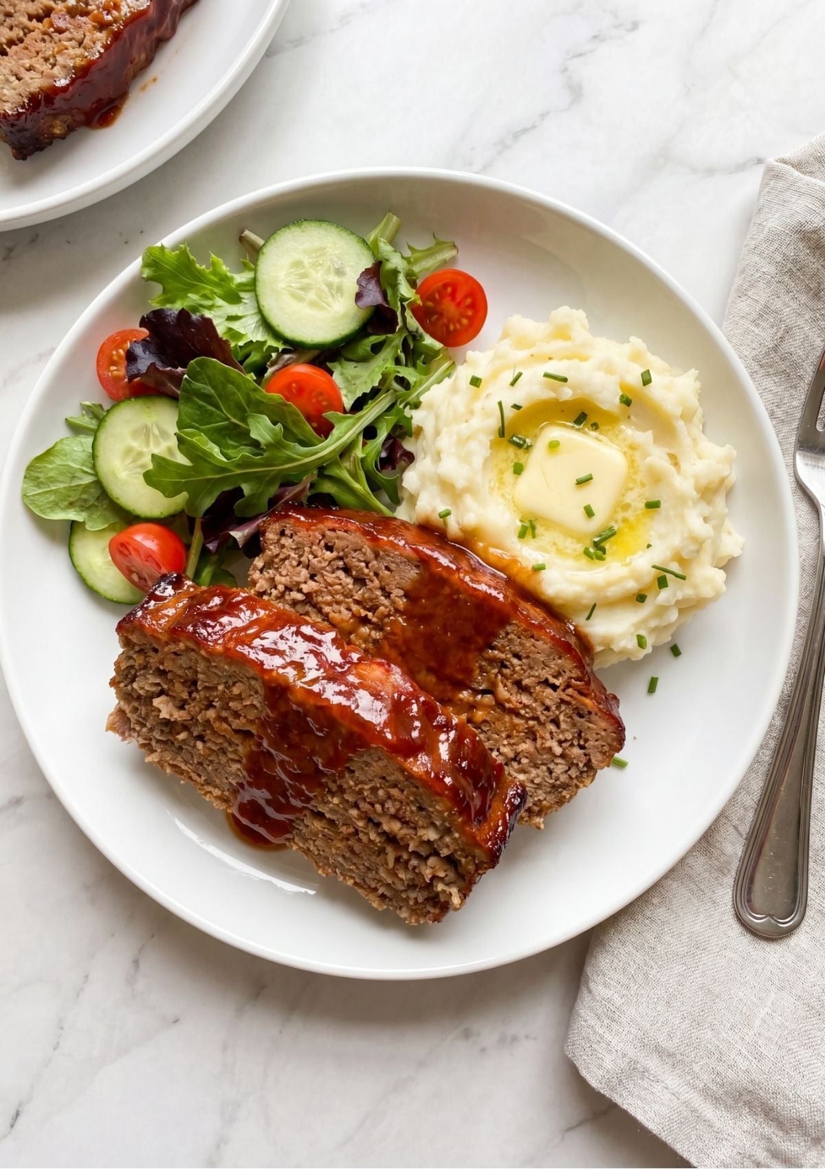 A white oval serving platter holding a whole glazed meatloaf with several thick slices cut at the end, revealing the moist interior texture and bits of white onion.