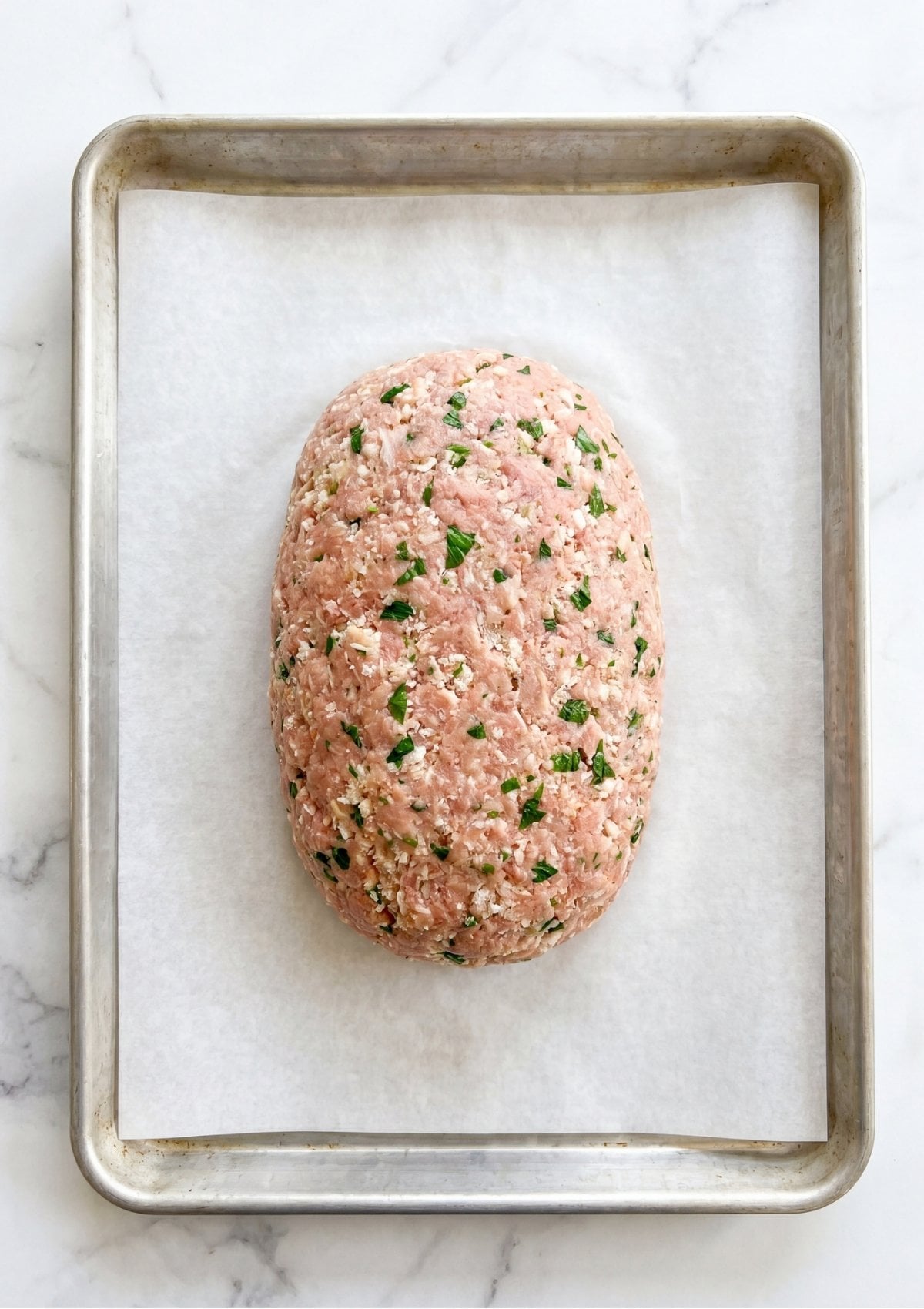 Overhead view of a raw turkey meatloaf shaped into an oval on a parchment-lined baking tray.
