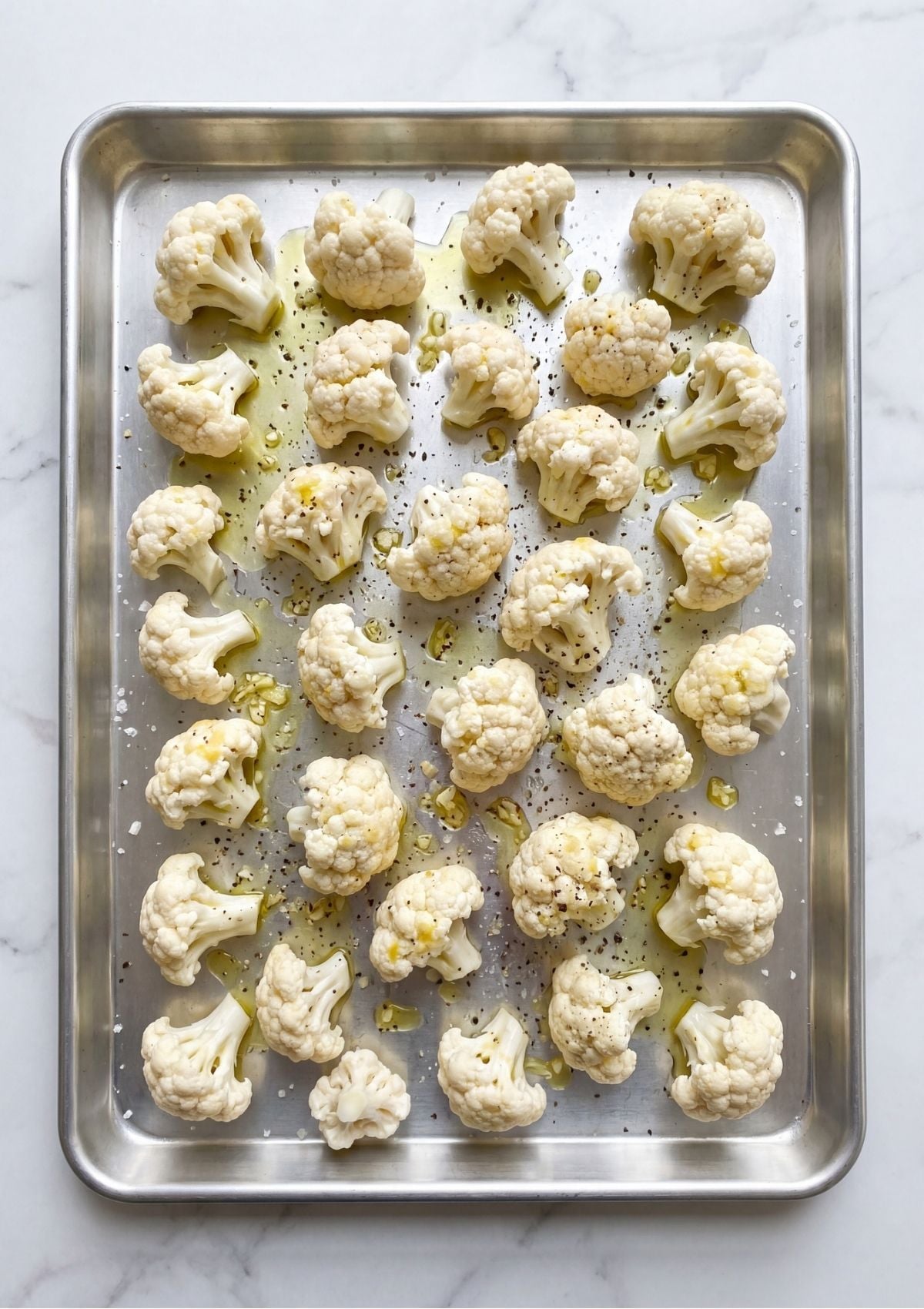 Cauliflower florets arranged in a single layer on a metal baking sheet drizzled with olive oil and seasoned with pepper and garlic