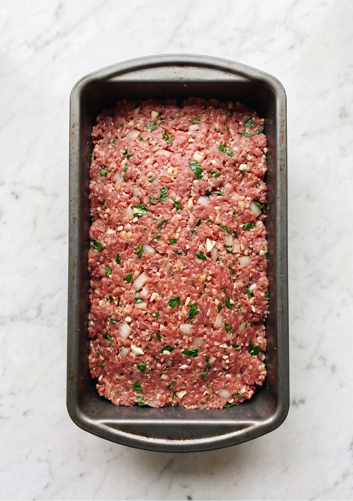 A large white mixing bowl containing ground beef combined with onions, breadcrumbs, herbs, and spices.