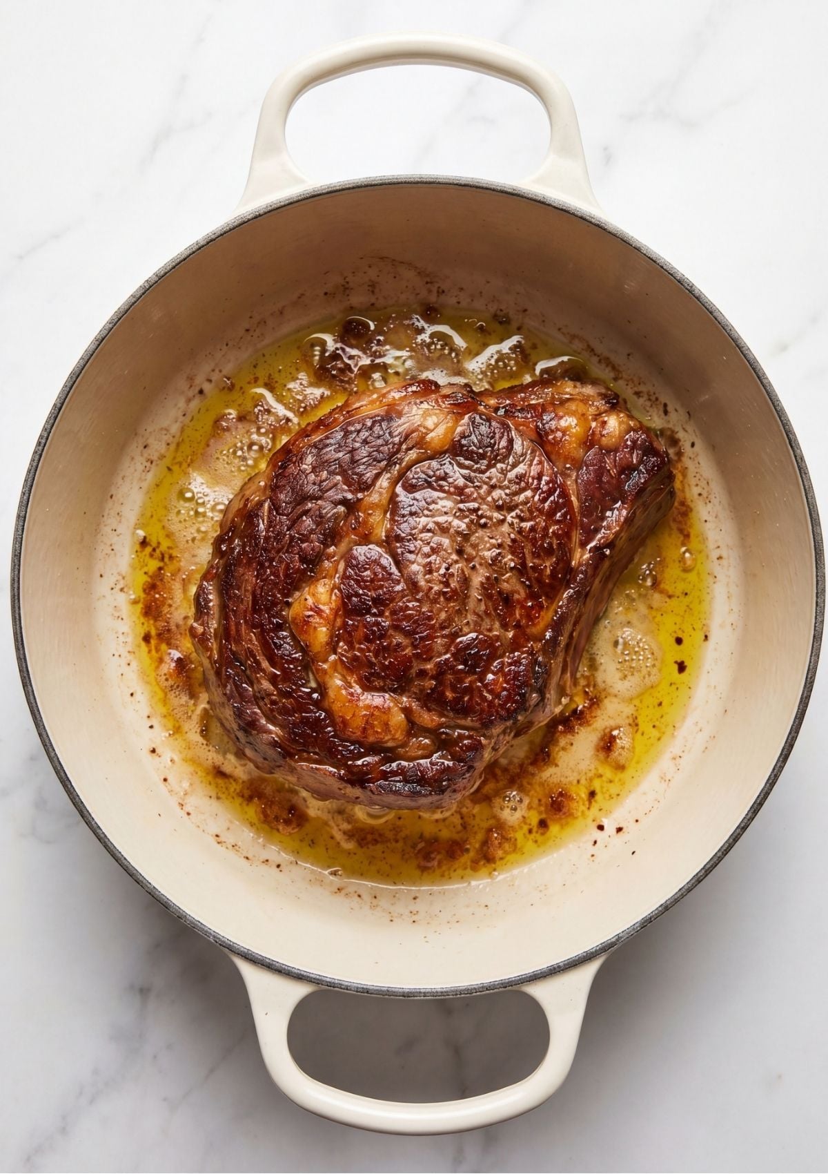 A beef arm roast searing until deeply browned in melted butter and olive oil inside a white Dutch oven.