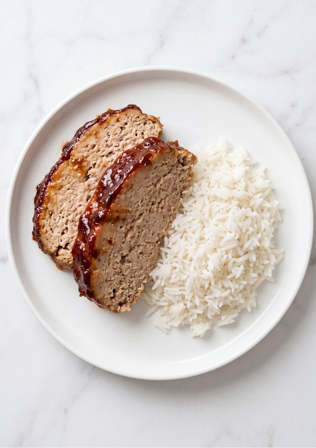 Two slices of glazed turkey meatloaf served on a white plate alongside a generous portion of fluffy white rice.