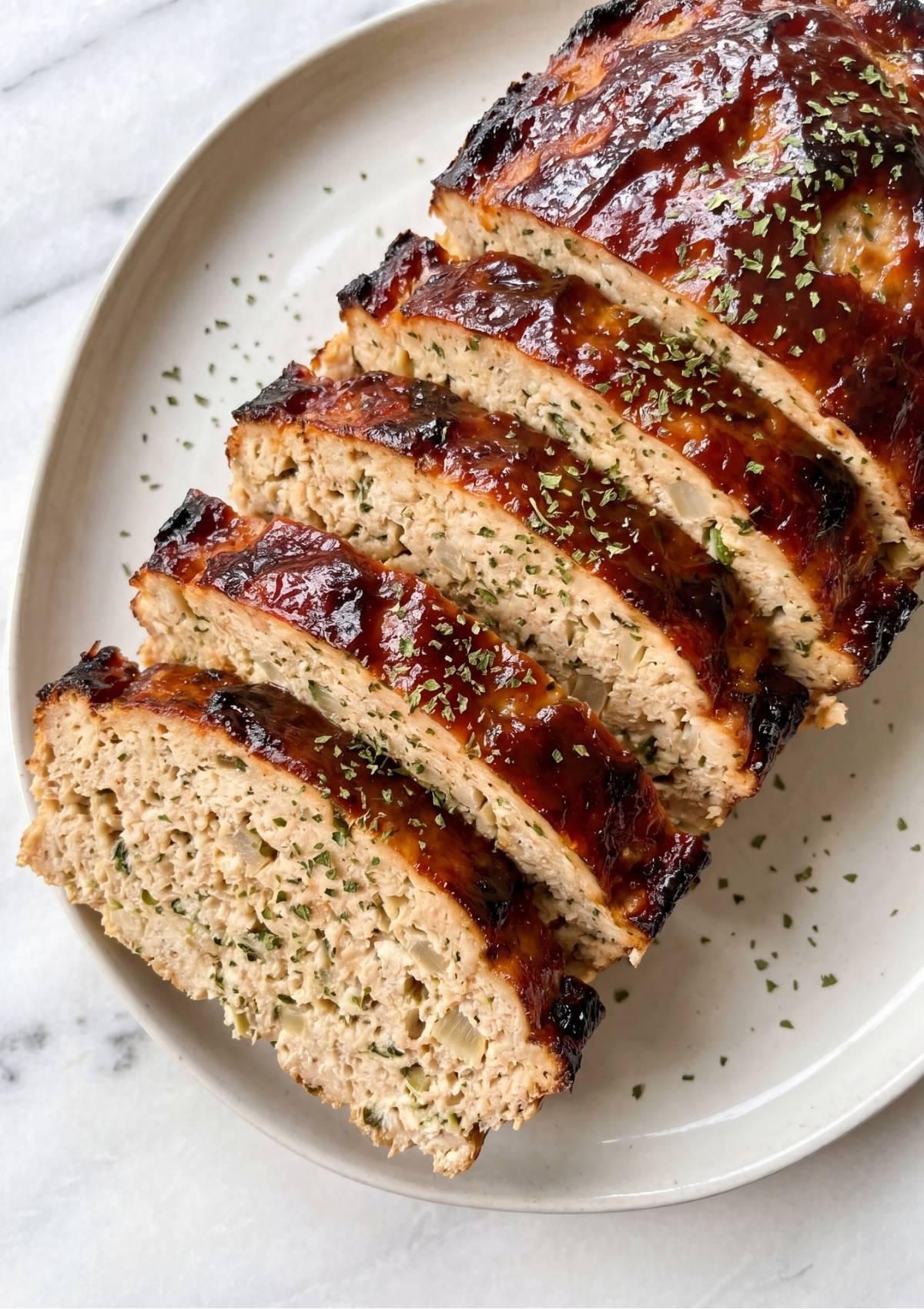 Angled view of sliced chicken meatloaf showing a tender interior and charred glaze edges garnished with parsley.