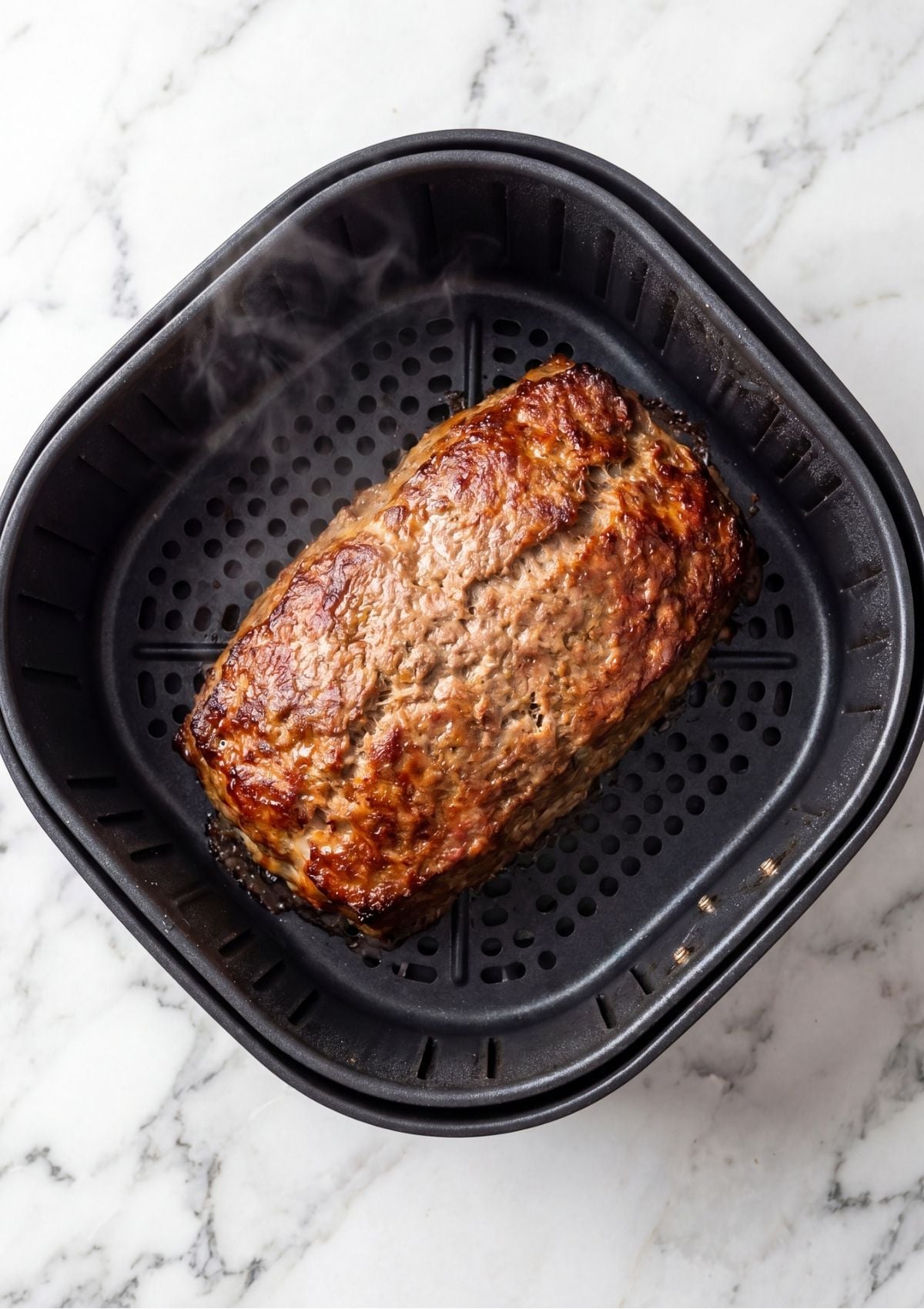 A cooked meatloaf without glaze sitting in a black air fryer basket showing a browned and textured surface.