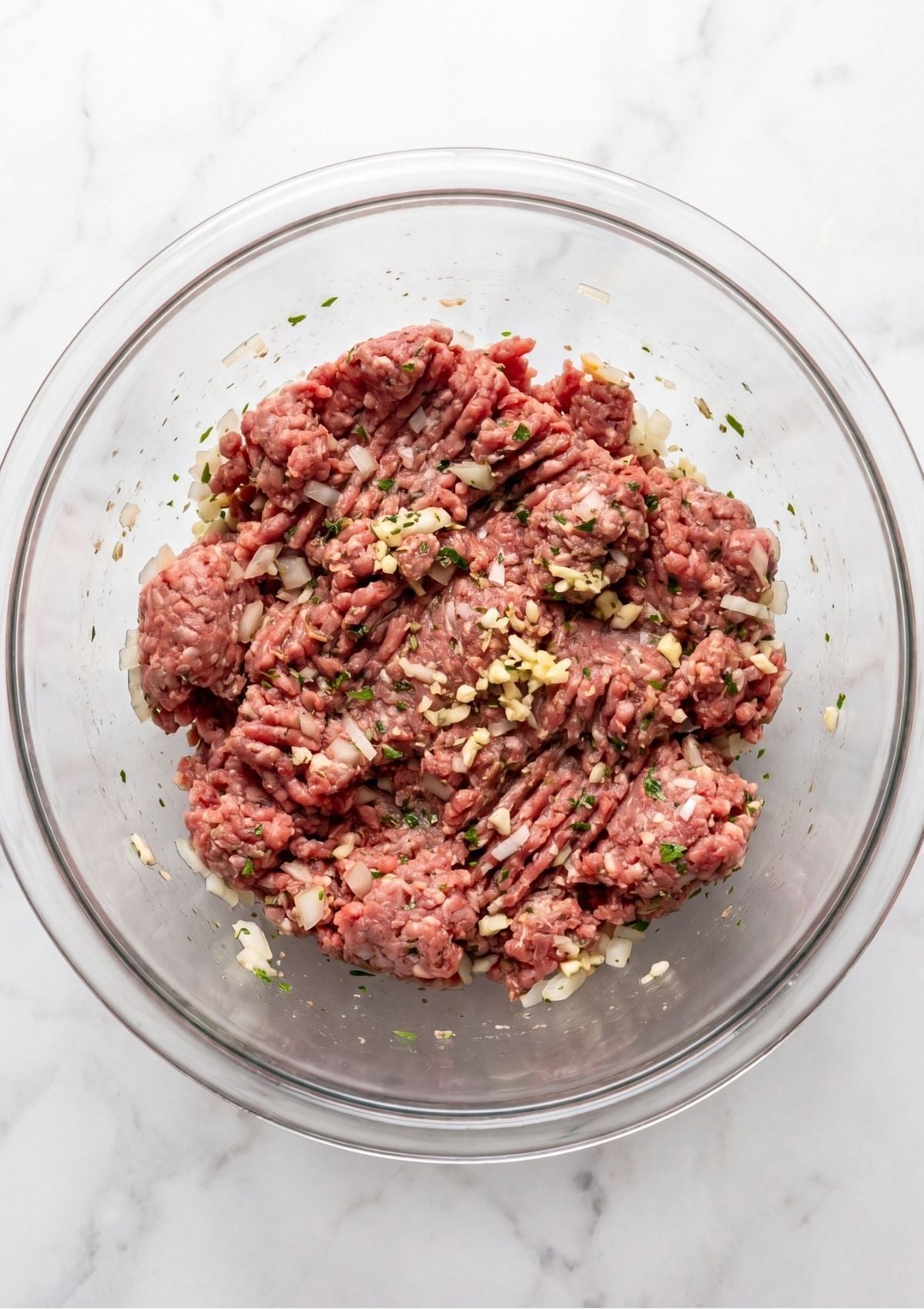 Raw meatloaf shaped into an oval loaf inside a white ceramic rectangular baking dish on a white background.