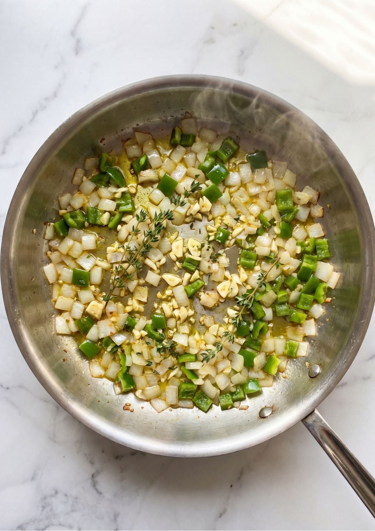 Diced onions and green bell peppers sautéing with fresh thyme in a stainless steel skillet