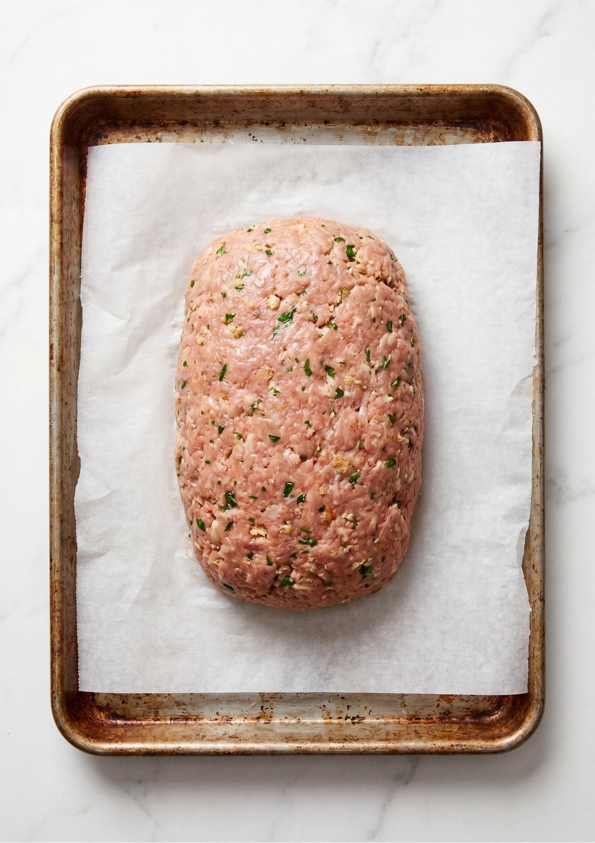 Raw ground turkey meatloaf shaped into an oval loaf on a baking sheet lined with white parchment paper.