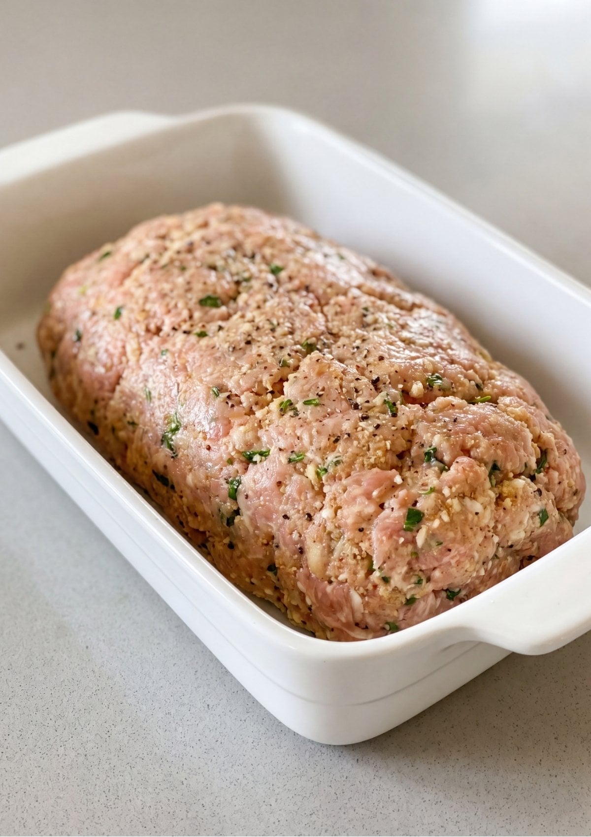 Raw seasoned ground turkey meatloaf mixture shaped into a neat loaf inside a white ceramic baking dish.