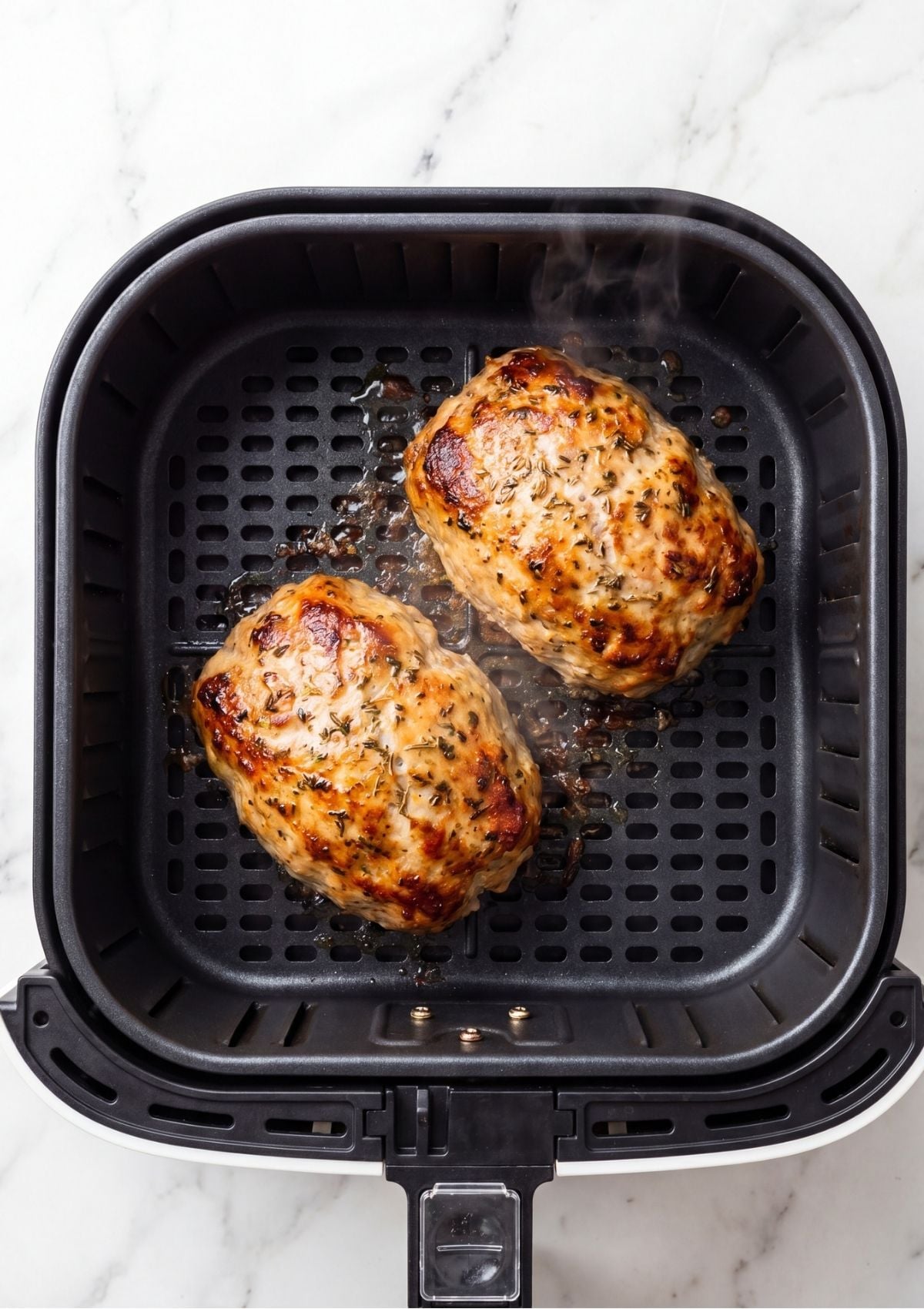 Two small turkey meatloaves browning inside a black air fryer basket with visible steam rising