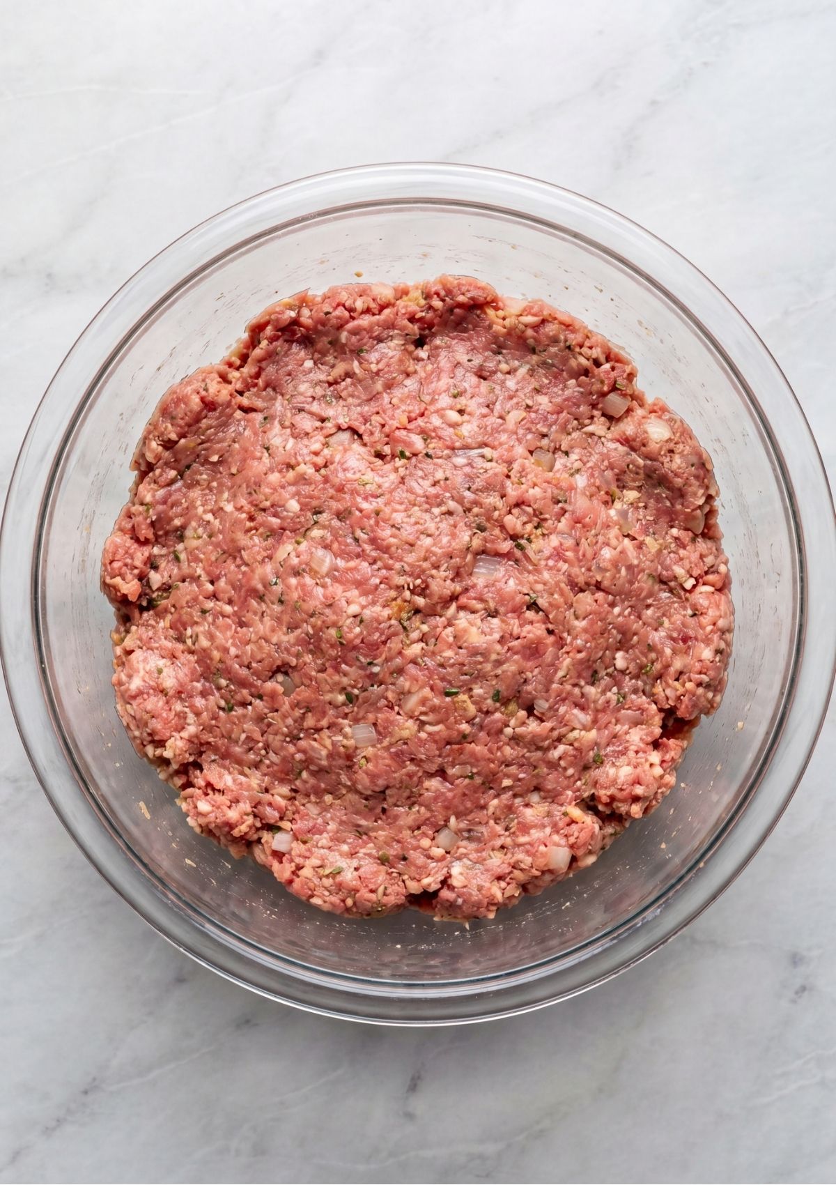 A clear glass bowl filled with the combined ground turkey, ground beef, egg, and breadcrumb mixture mixed together.