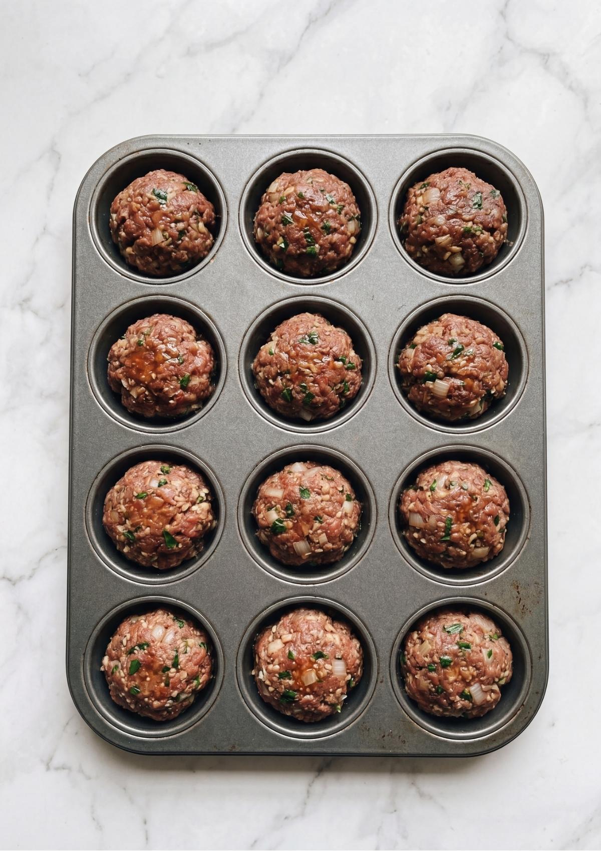 Raw meatloaf mixture scooped into a 12-cup muffin tin before baking.