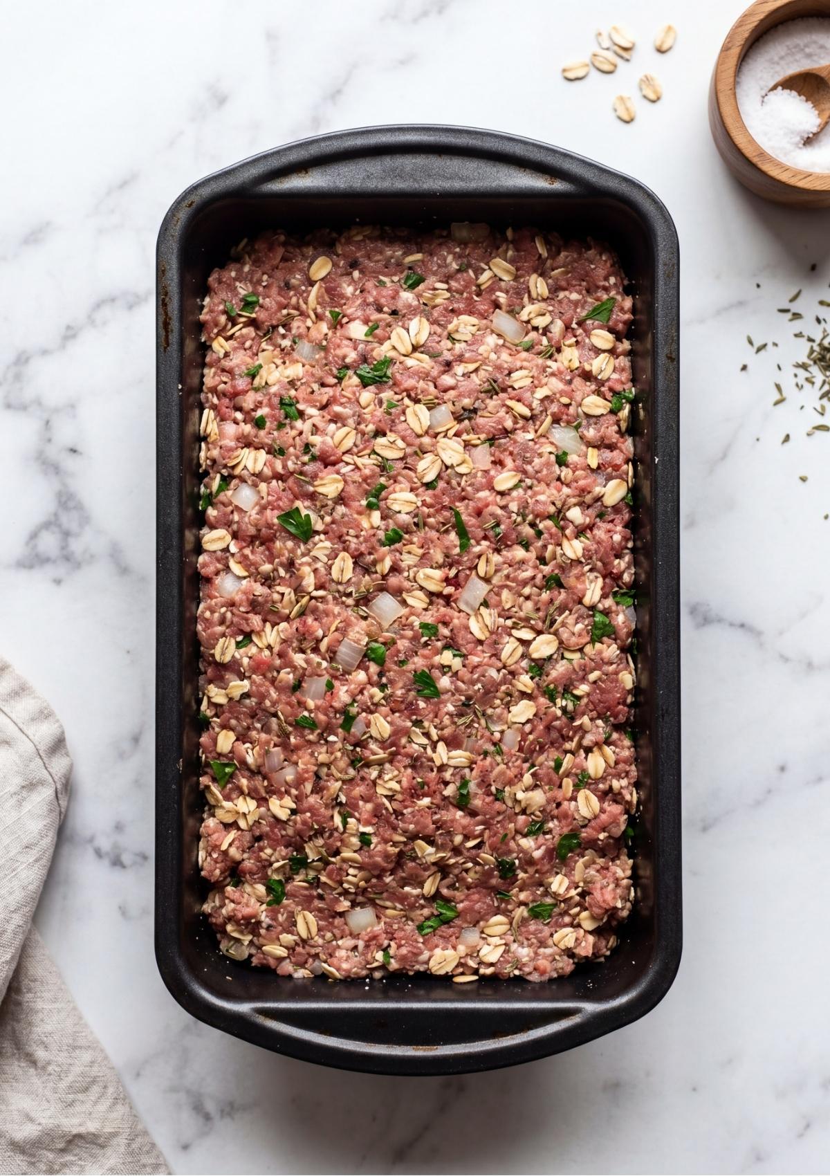 Uncooked meatloaf in a pan topped with a generous, smooth layer of red glaze.