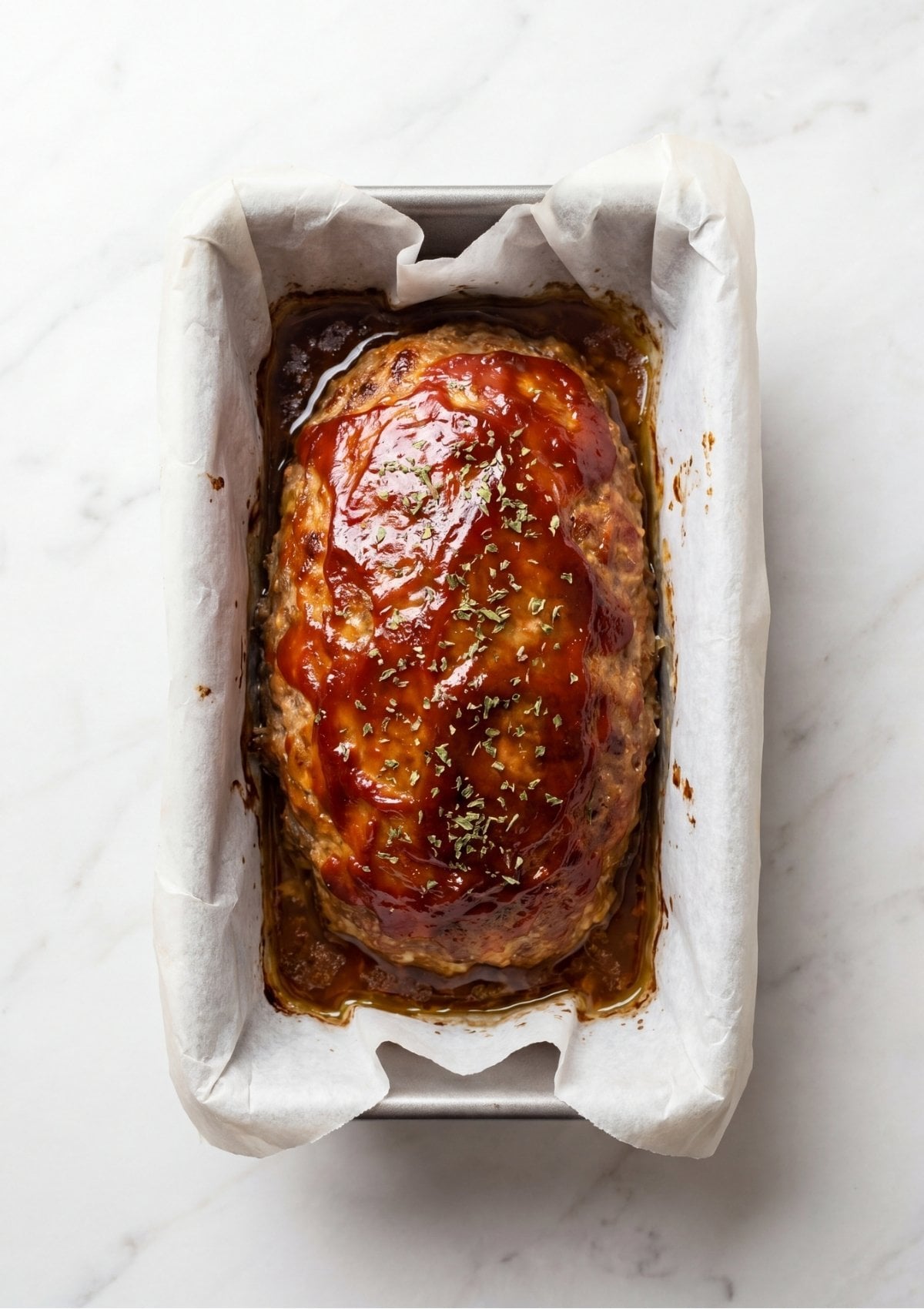 A golden-brown baked meatloaf covered in a bubbling tomato glaze sitting in a parchment-lined loaf pan fresh from the oven.