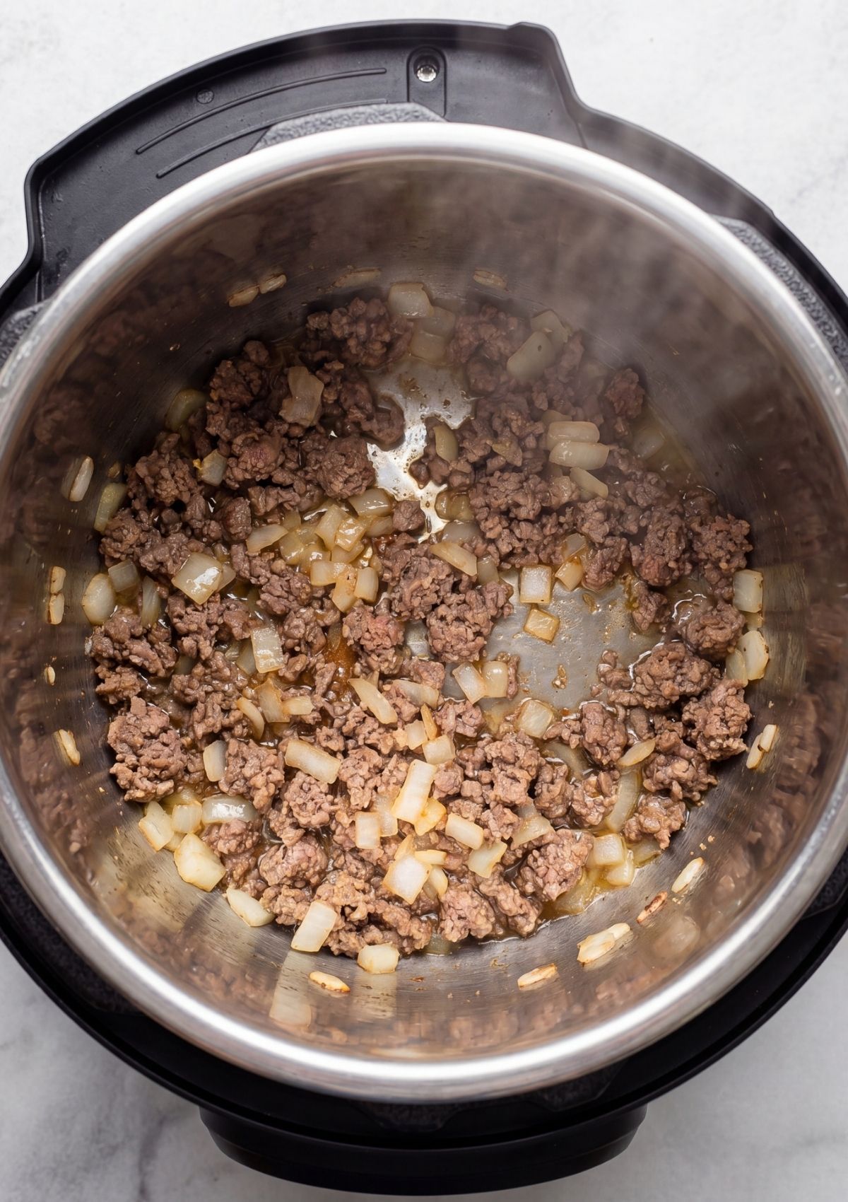 Ground beef and diced onions being sautéed together in the stainless steel inner pot of an Instant Pot.