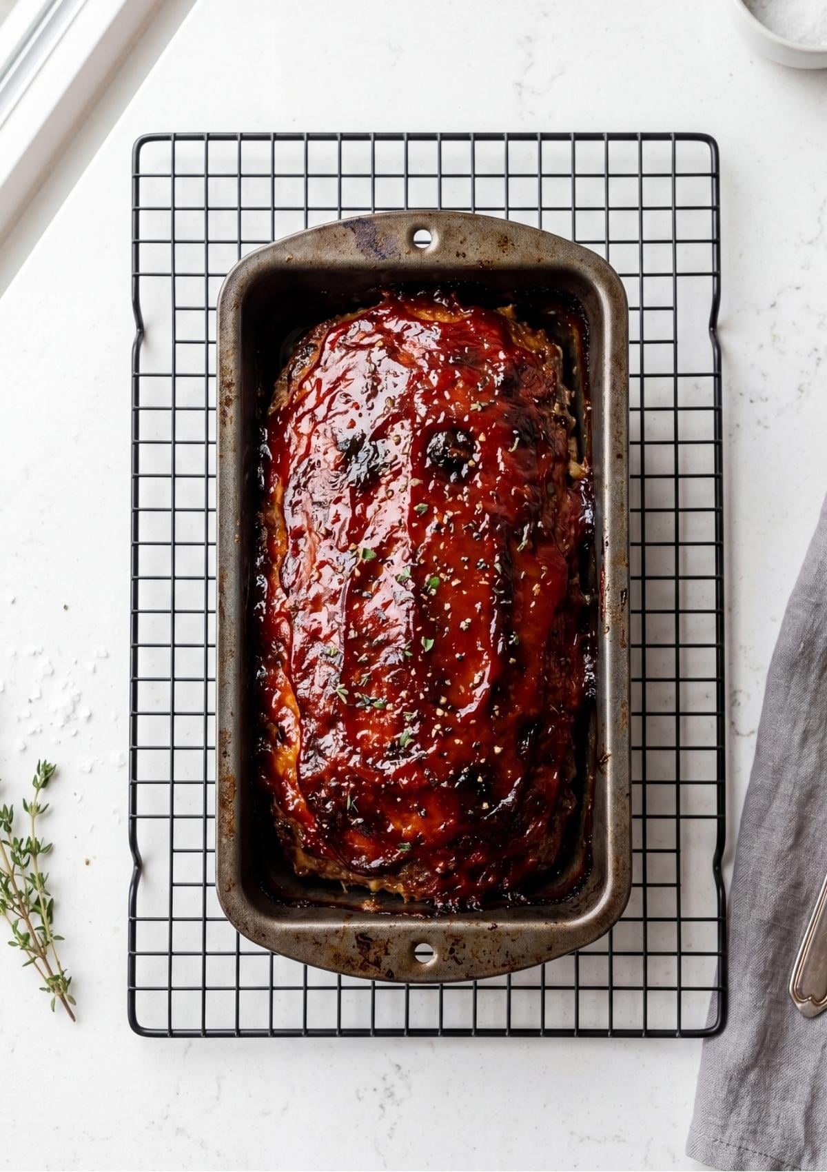A swirl of tomato-based glaze being applied to the top of the raw meatloaf in a loaf pan.