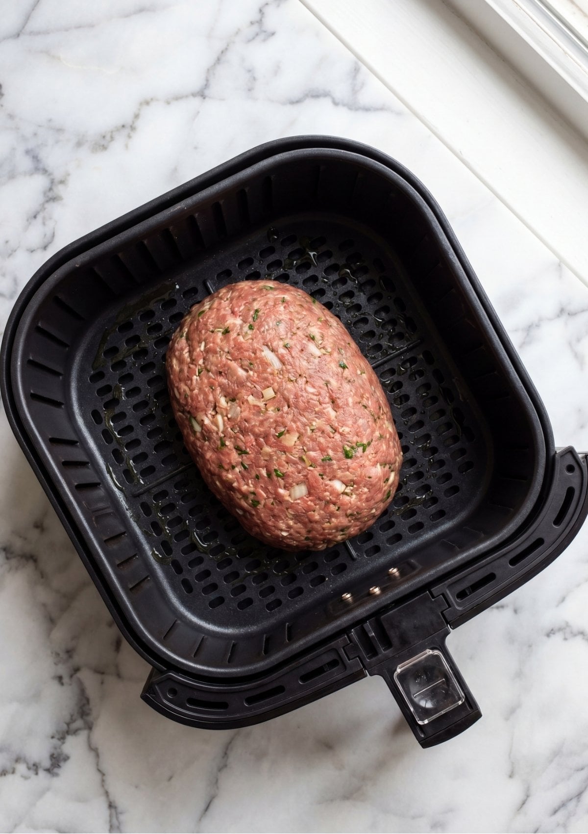 Raw meatloaf mixture shaped into a neat oval loaf resting inside a black air fryer basket.