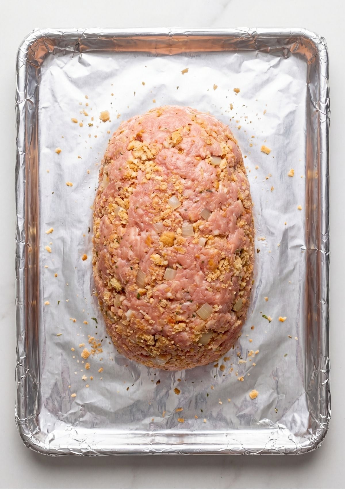A raw ground turkey meatloaf shaped into an oval on a foil lined baking sheet before being placed in the oven.