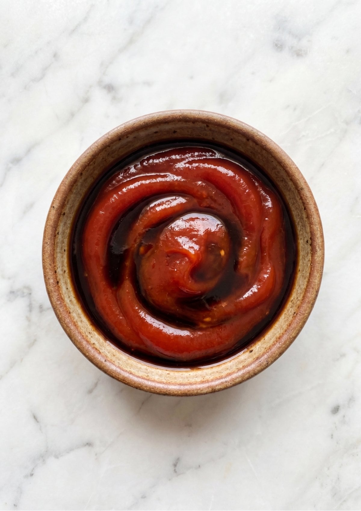 Top-down view of a small ceramic bowl containing thick red ketchup swirled with dark brown Worcestershire sauce
