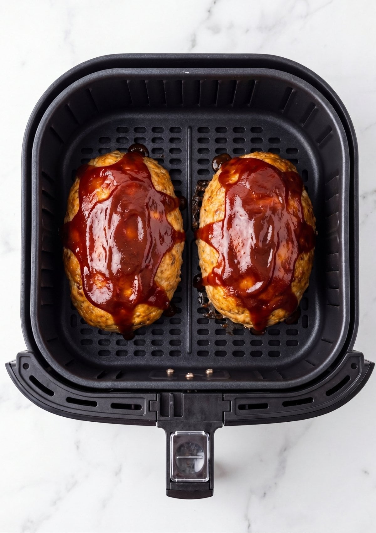 Two cooked turkey meatloaves topped with a thick, dark red ketchup glaze sitting inside a black air fryer basket
