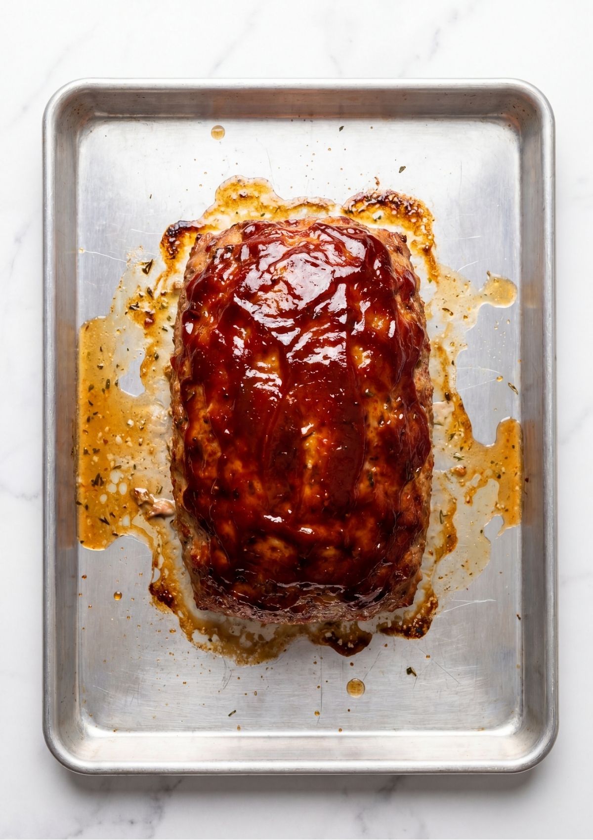 A whole baked turkey meatloaf with a sticky caramelized ketchup glaze resting on a rimmed baking sheet pan