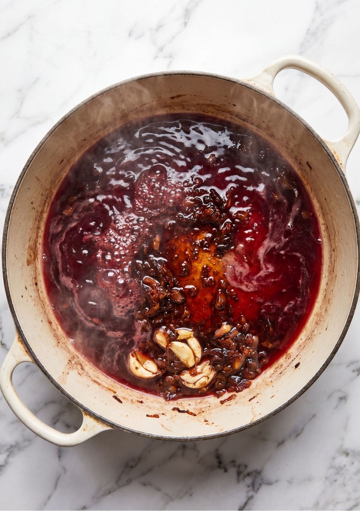 Red wine simmering and bubbling with sautéed garlic and browned bits in a white Dutch oven to deglaze the pan.