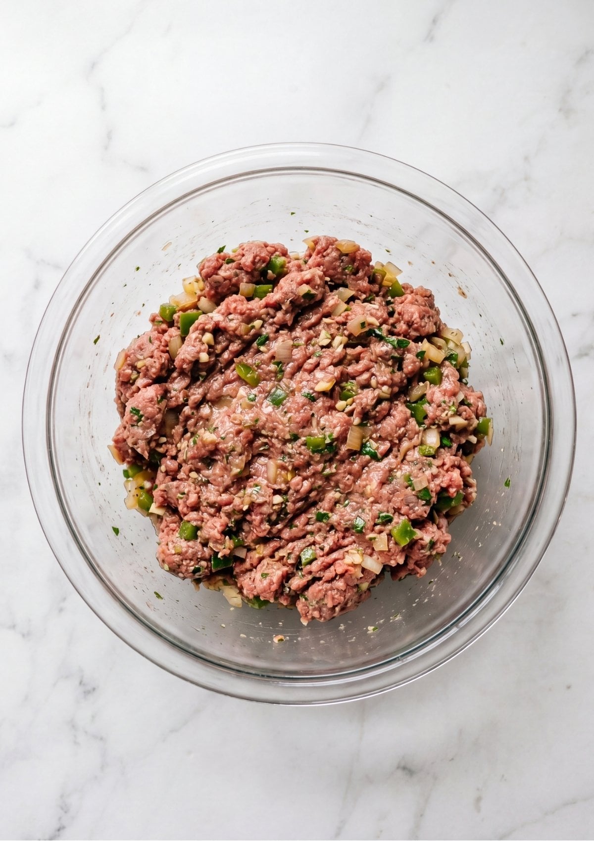 The meatloaf mixture fully combined with onions, peppers, and herbs in a glass bowl, ready to be shaped for baking.