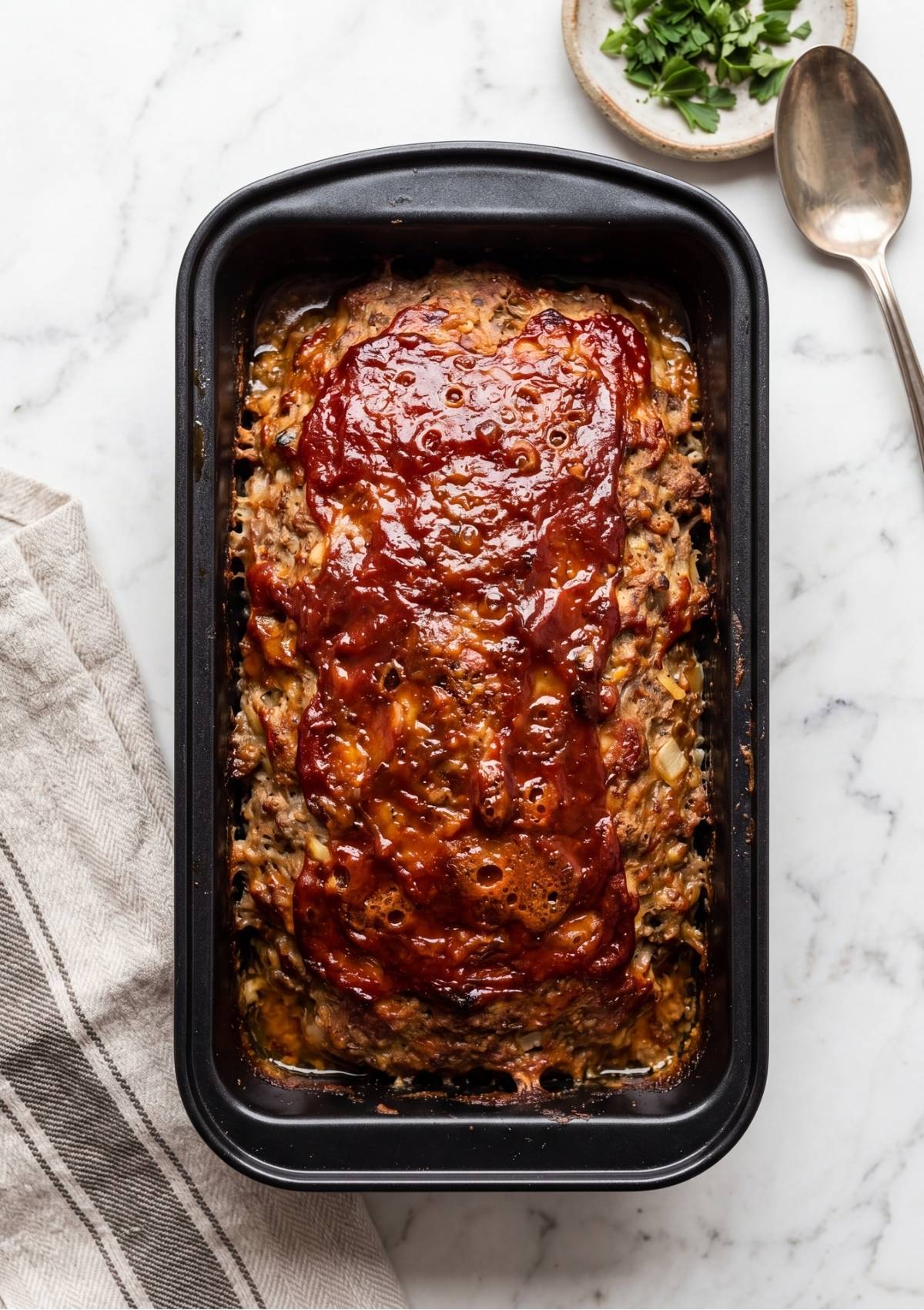 A cooked meatloaf in a loaf pan with a bubbling, caramelized red glaze.