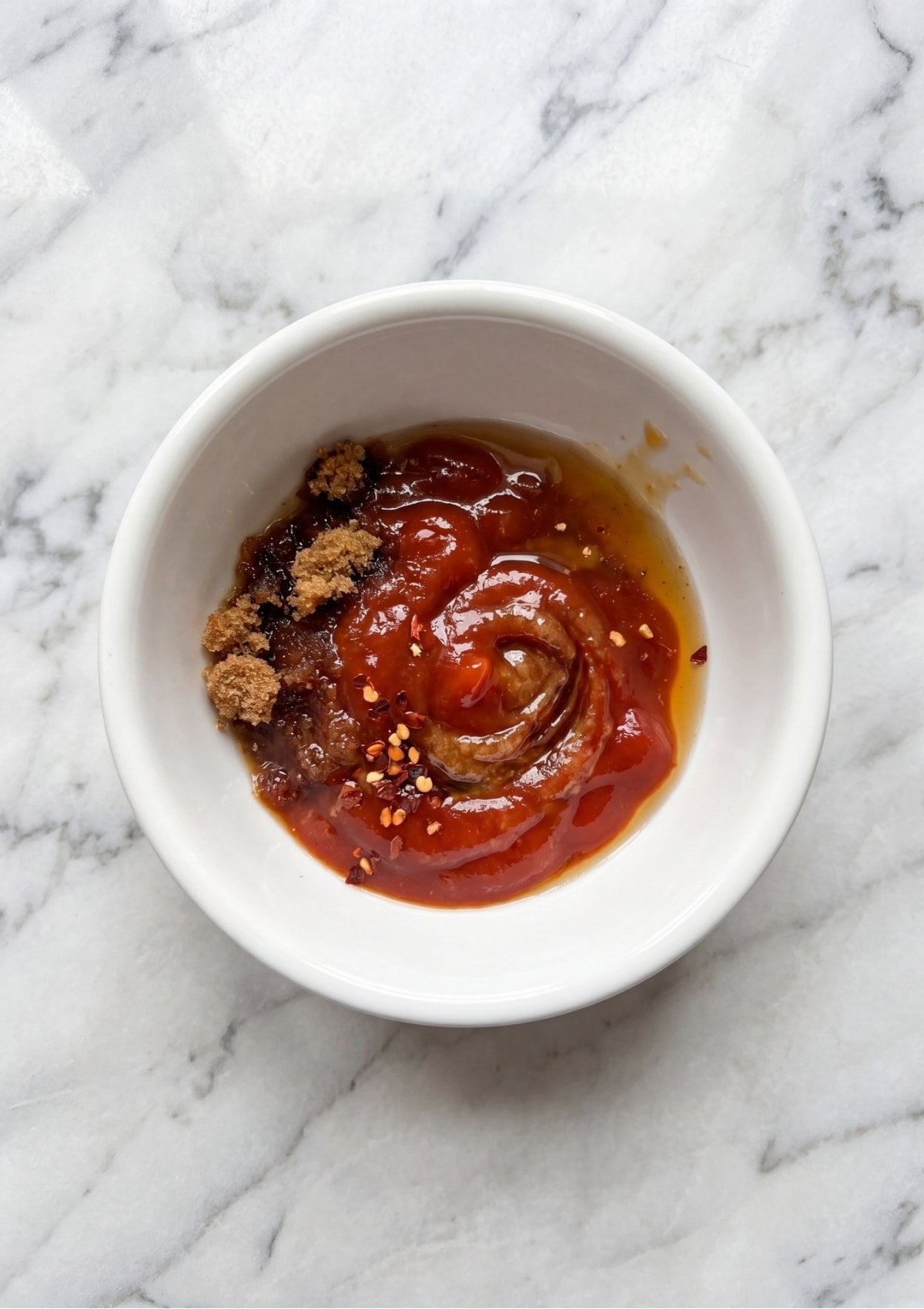 A small white bowl containing a mixture of ketchup, brown sugar, apple cider vinegar, and red pepper flakes for a sweet and tangy glaze.