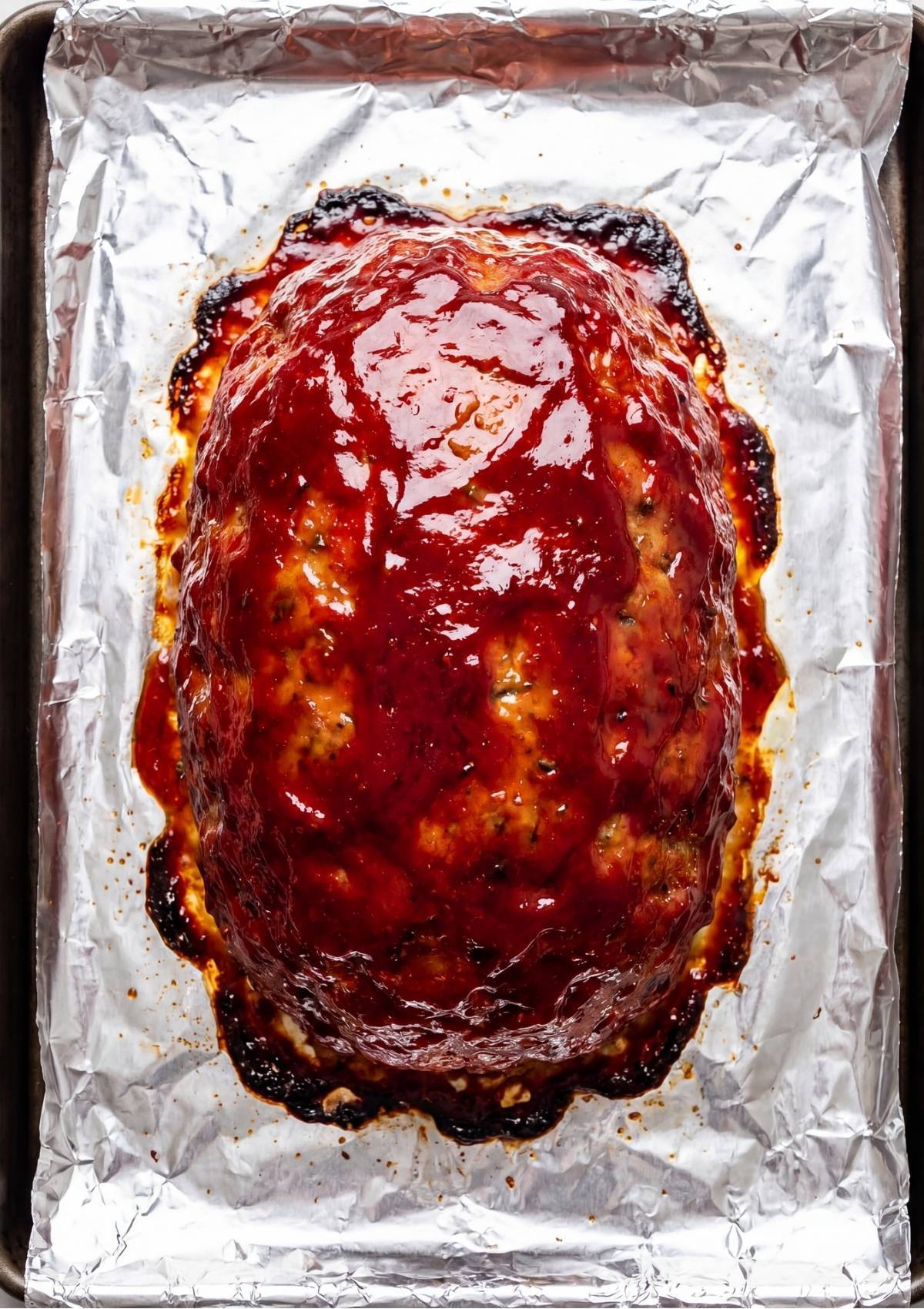 A cooked turkey meatloaf topped with a thick red glaze sitting on a parchment lined baking sheet.