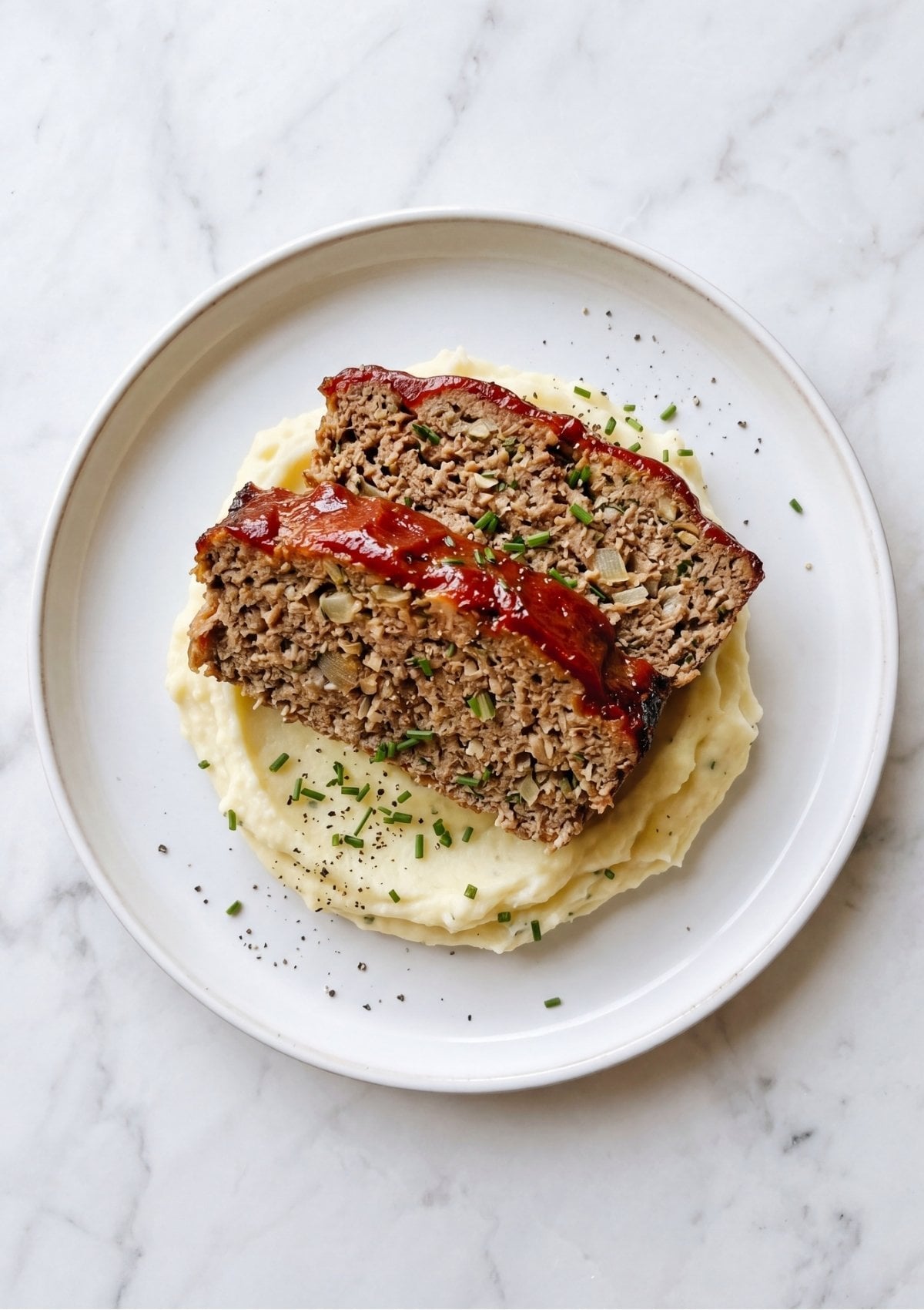 Two thick slices of glazed meatloaf seasoned with chives served over a bed of creamy mashed potatoes for an easy meatloaf recipe meal.