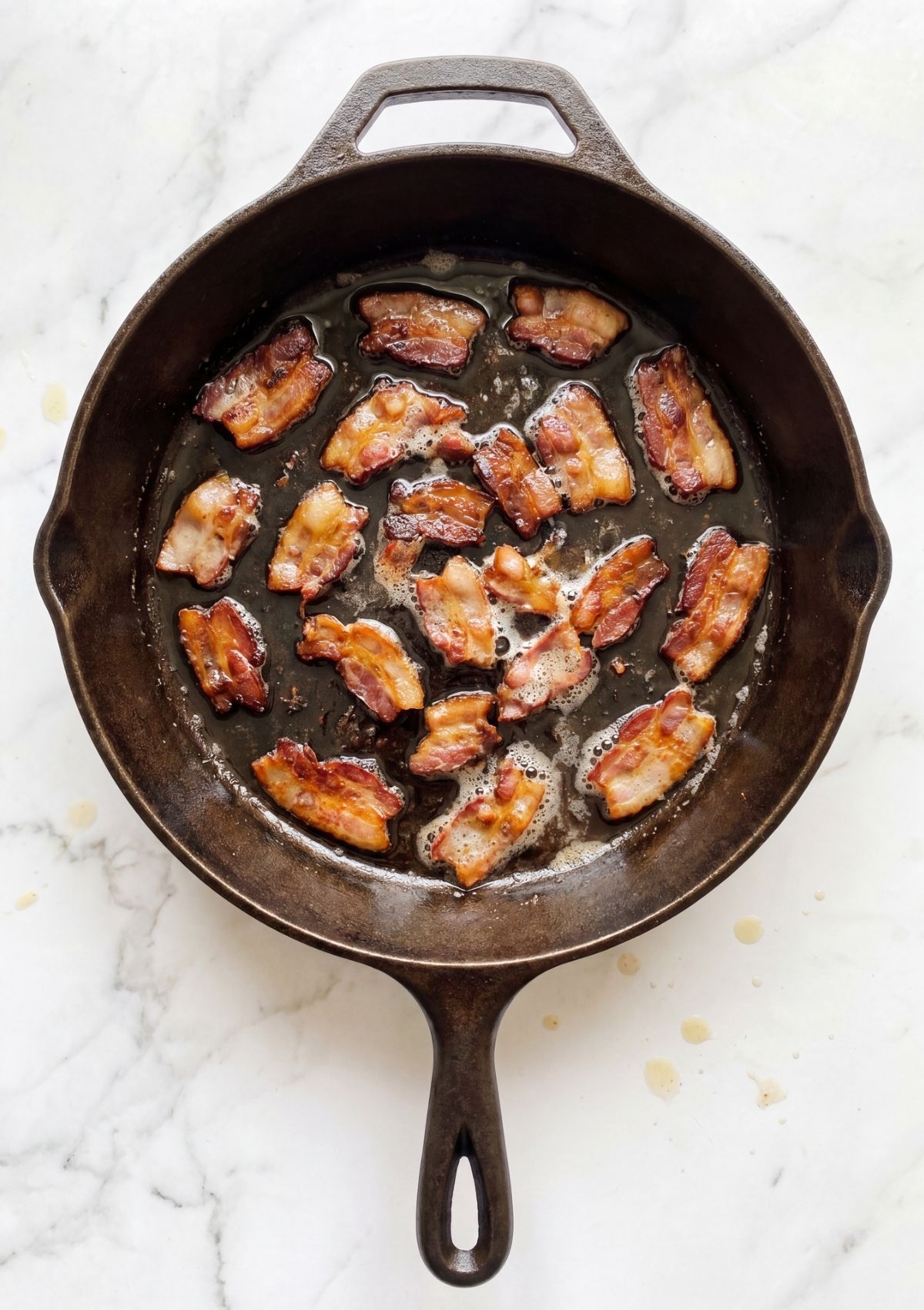 Chopped bacon pieces frying in a cast iron skillet until golden brown and crispy.