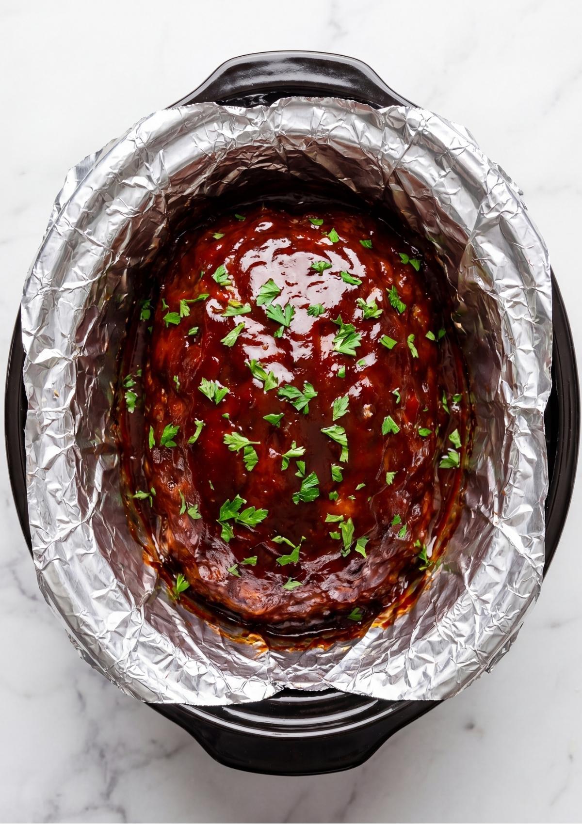 Top down view of a glazed meatloaf in a crockpot garnished with chopped fresh parsley