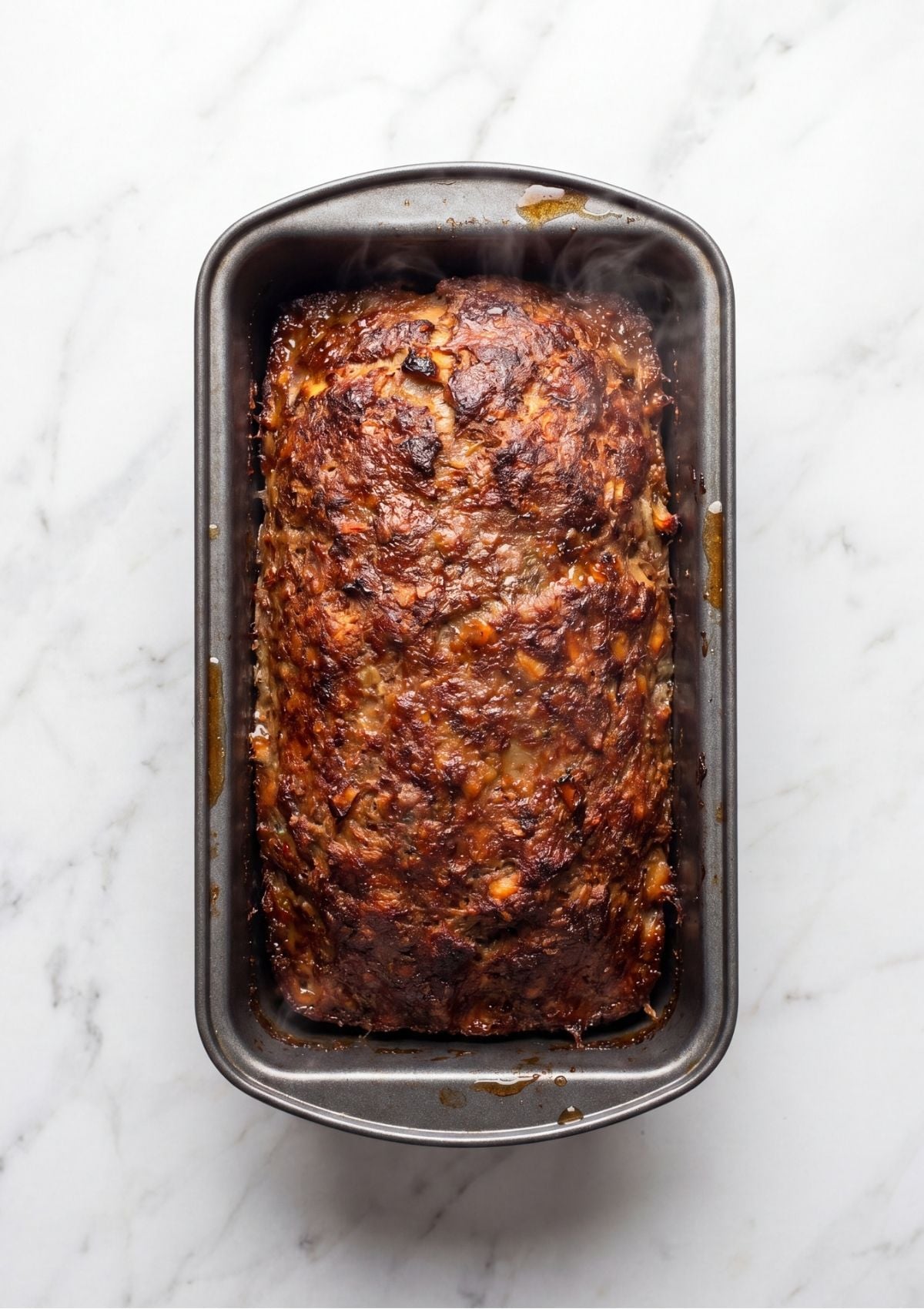 A fully baked, golden brown turkey and beef meatloaf resting inside a dark metal loaf pan right out of the oven.