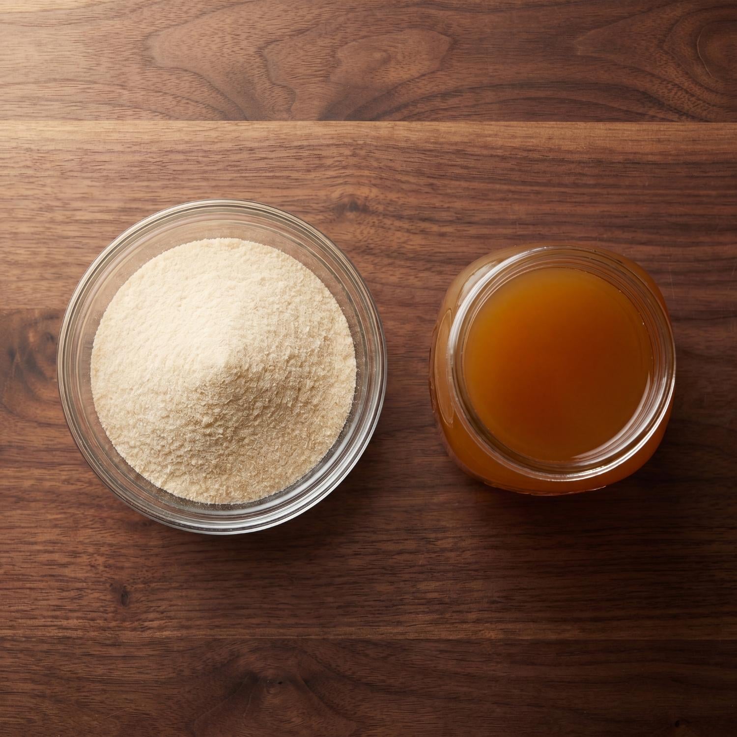 Bowl of beef gelatin powder next to a glass of bone broth on a wooden kitchen counter