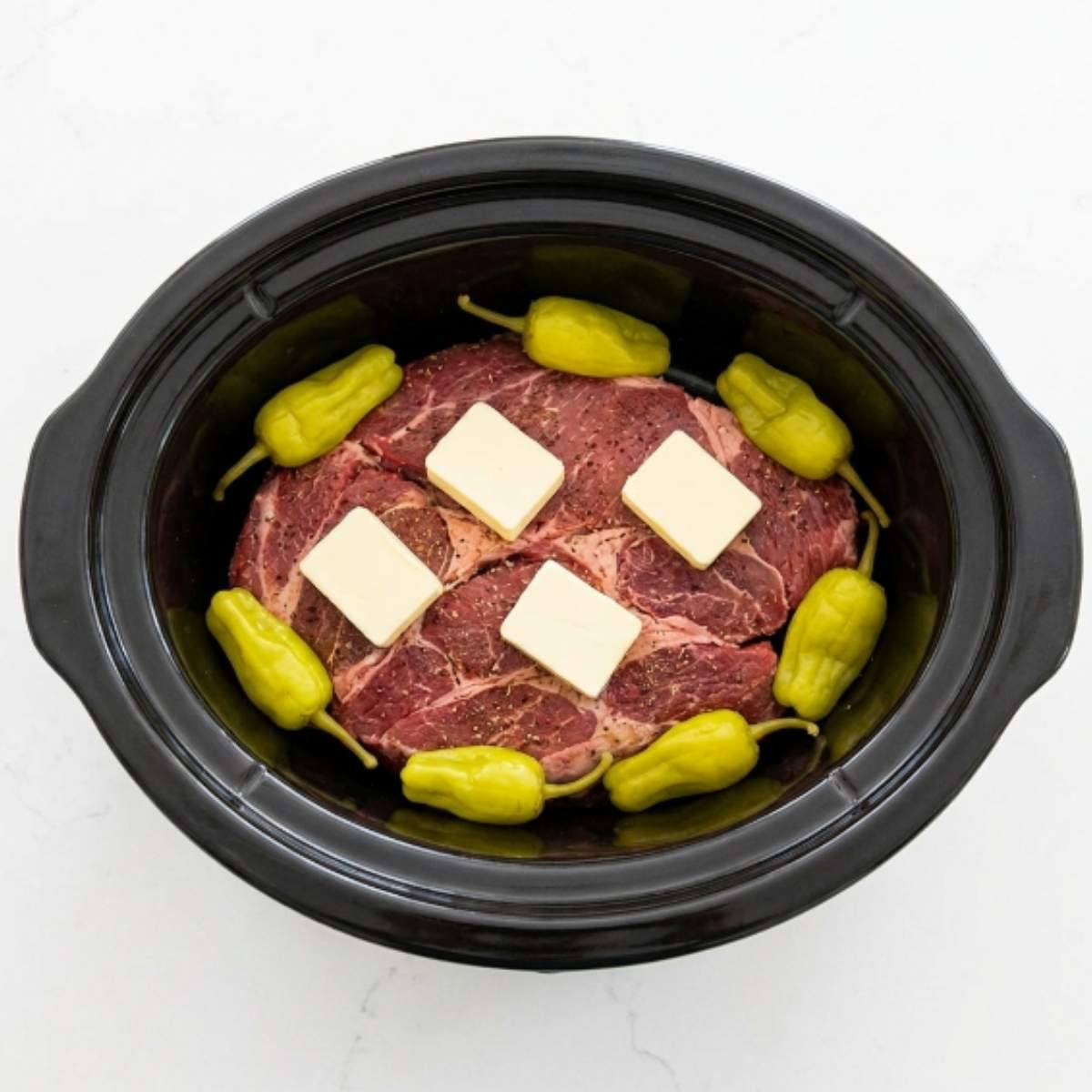 raw-seasoned-chuck-roast-topped-with-butter-pats-and-surrounded-by-pepperoncini-peppers