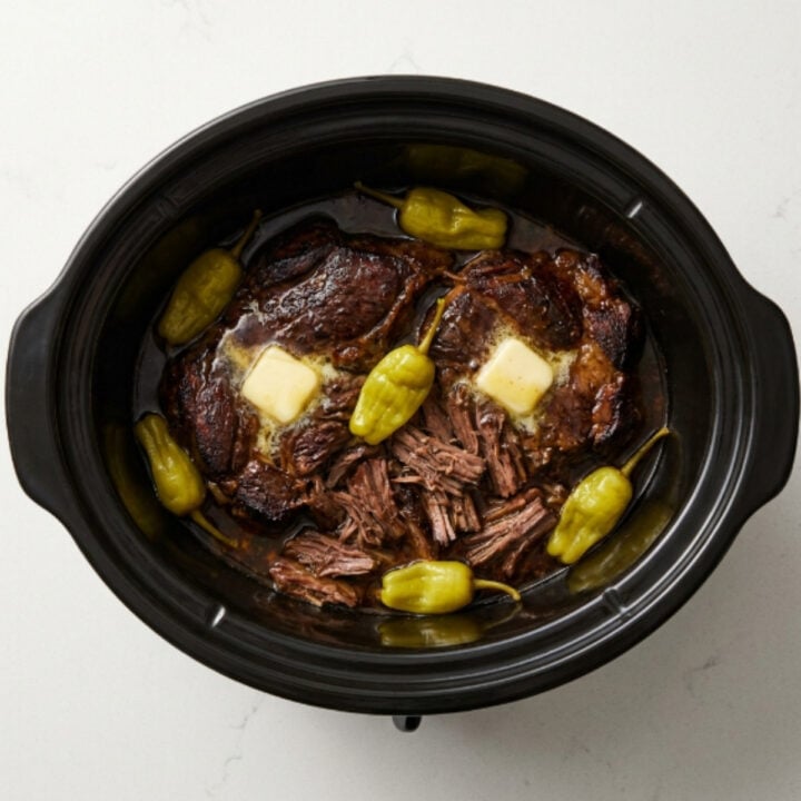 overhead-view-of-cooked-shredded-mississippi-pot-roast-in-a-slow-cooker-with-pepperoncini-peppers