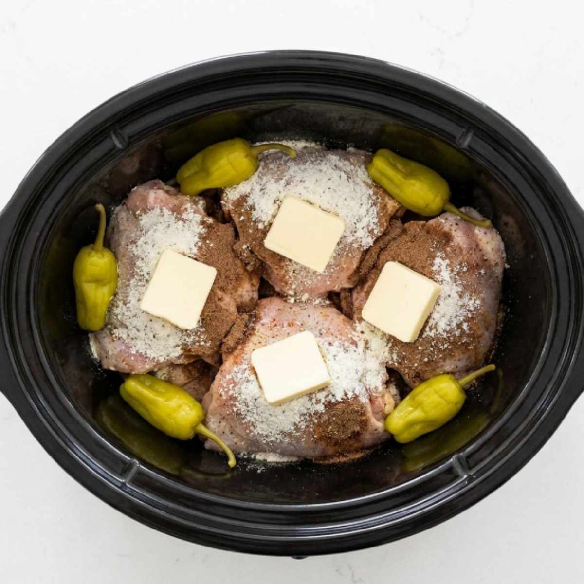 raw-bone-in-chicken-thighs-in-a-slow-cooker-topped-with-ranch-seasoning-butter-pats-and-pepperoncini