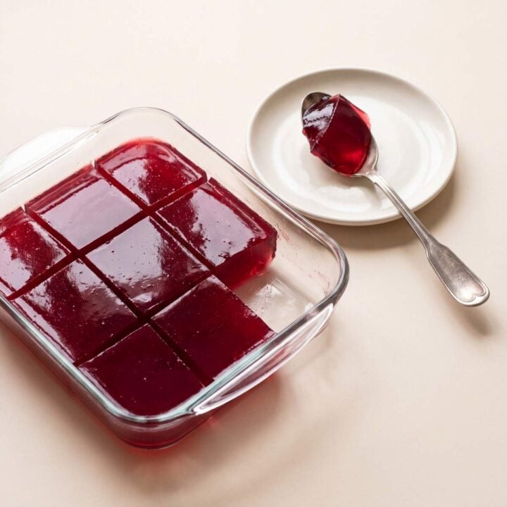 Homemade beef collagen jello cut into glossy red squares with a serving spoon on a small plate