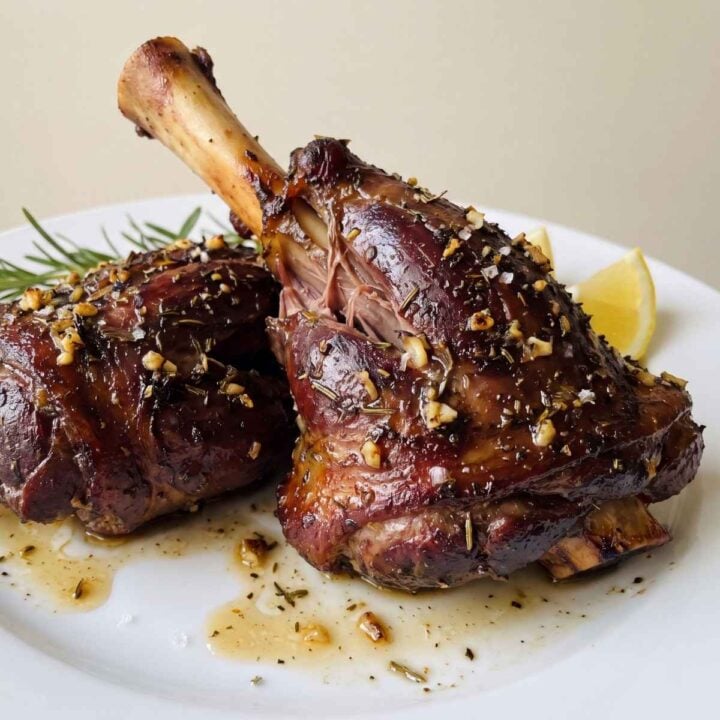 Roast lamb shanks in air fryer plated with lemon wedges and fresh rosemary