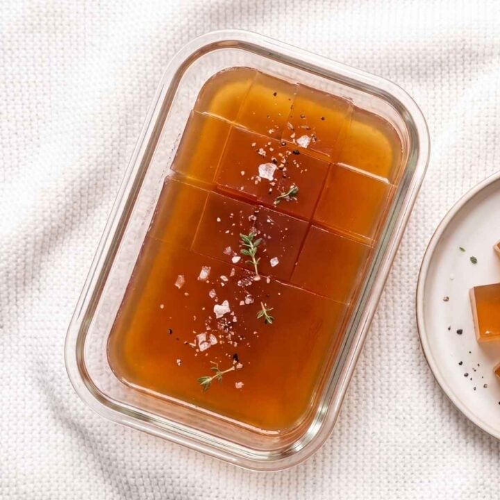 Close-up of set beef jelly sliced into squares in a glass container, garnished with sea salt and thyme